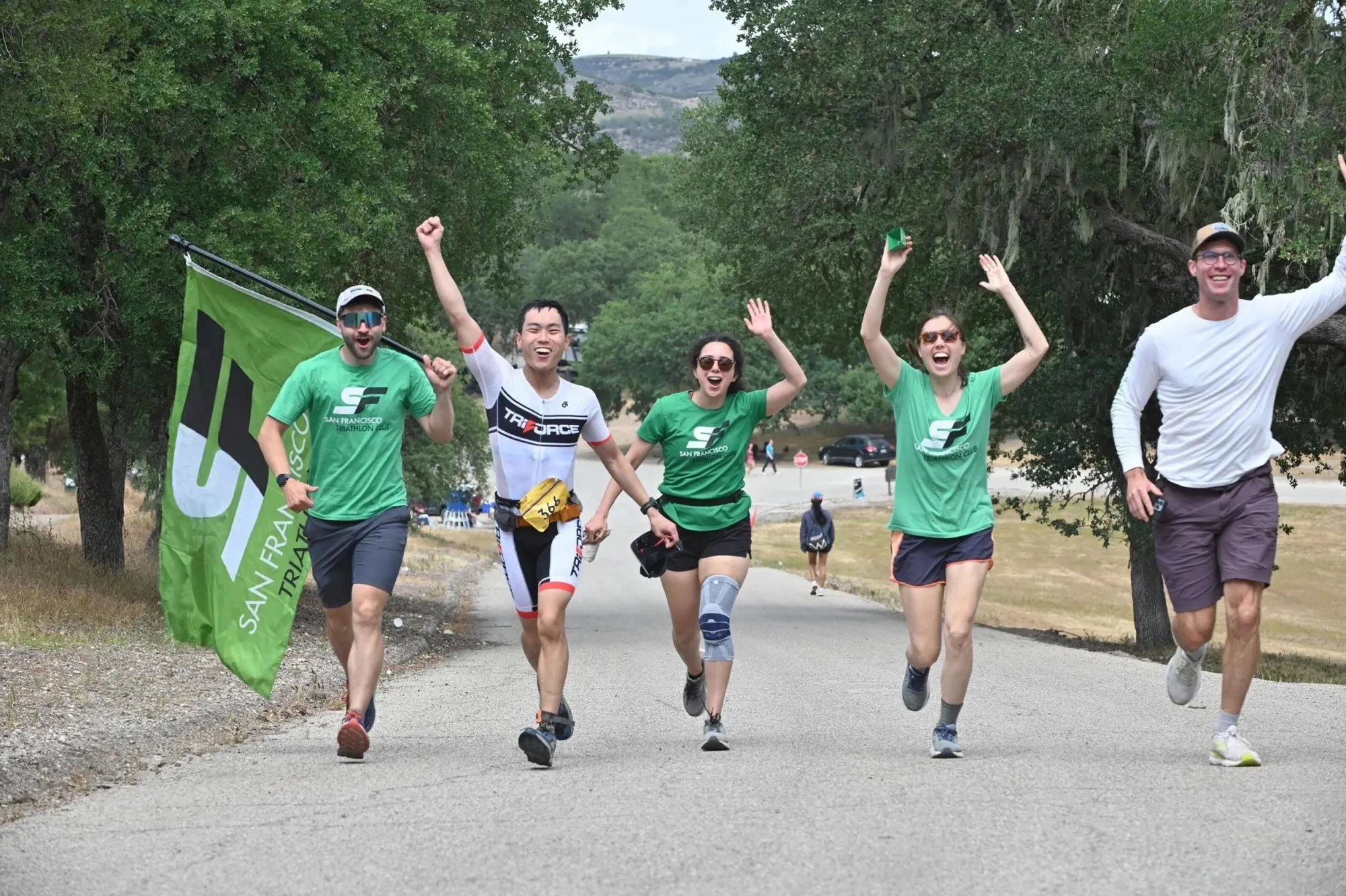 SF Tri Club members in club shirts running and cheering with the club flag